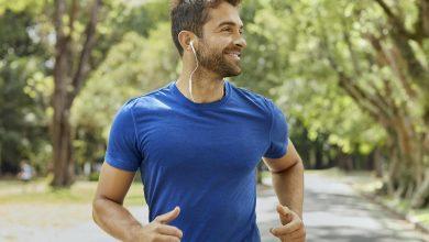 5 راز سلامتی برای مردان 40 سال به بالا 2 مردی خندان با تی شرت آبی در یک پارک در حال دویدن است.