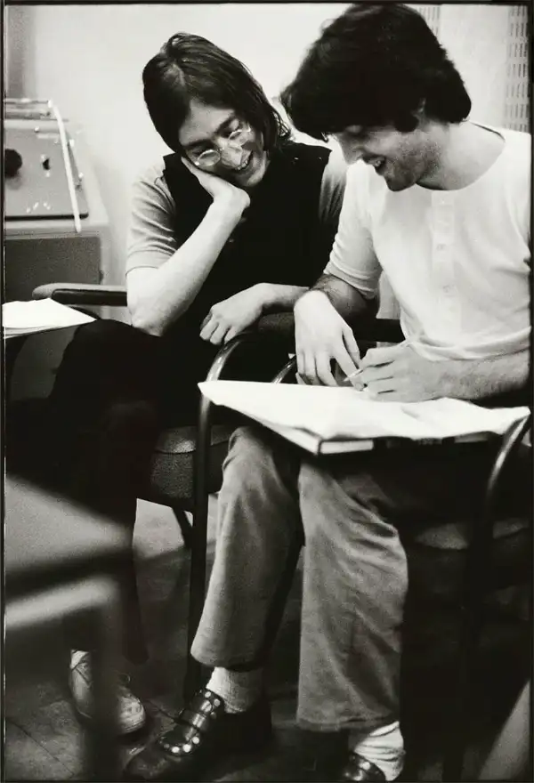 جان لنون و پل مک کارتنی کنار هم روی صندلی نشسته اند و به یک دفتر نگاه می کنند