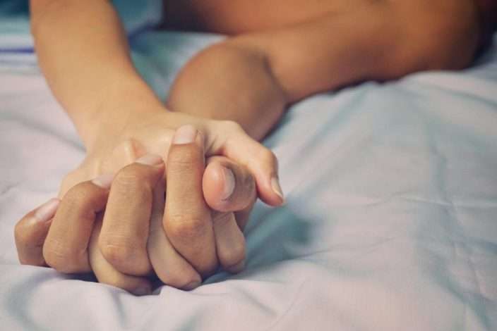 روی یک تخت با ملحفه سفید، دست خوابیده یک مرد در دست یک زن دیده می شود که نشان دهنده رابطه جنسی میان آنها است.