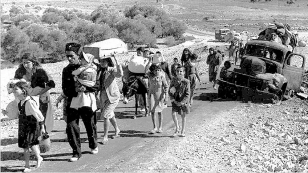زنان و مردان و کودکان فلسطینی که آواره شده اند در جاده ای از کنار یک ماشین خراب عبور می کنند.